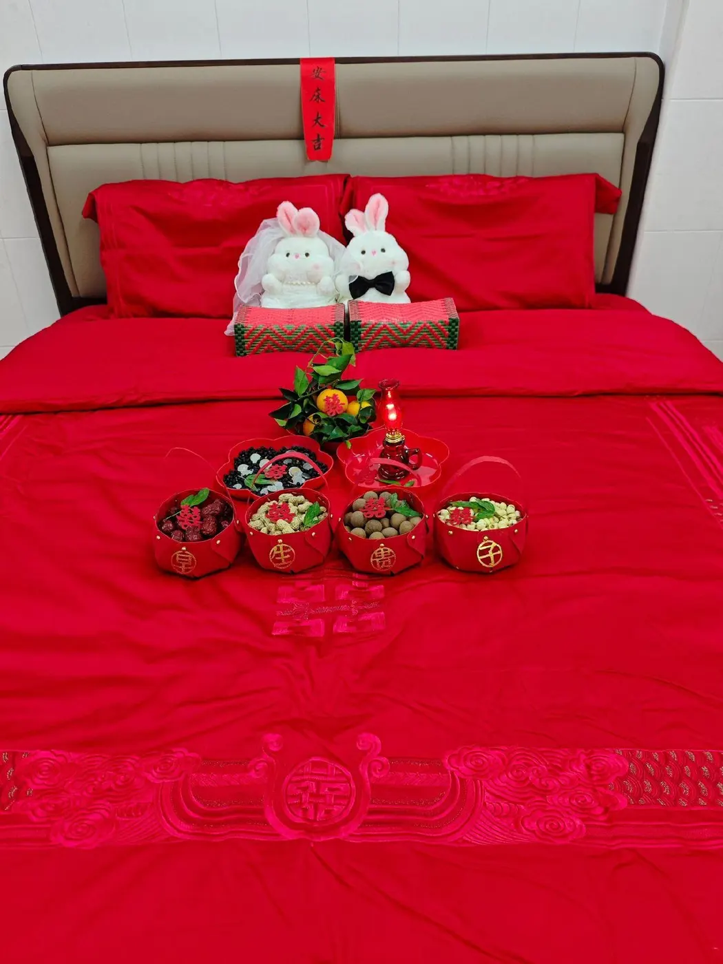 婚床铺红被，两个兔形压床娃娃靠在枕上，床前摆五果和糖果，床头贴一张「安床大吉」红纸。图源：抖音 @囍結良緣婚嫁一站式，2022 年 10 月 17 日。