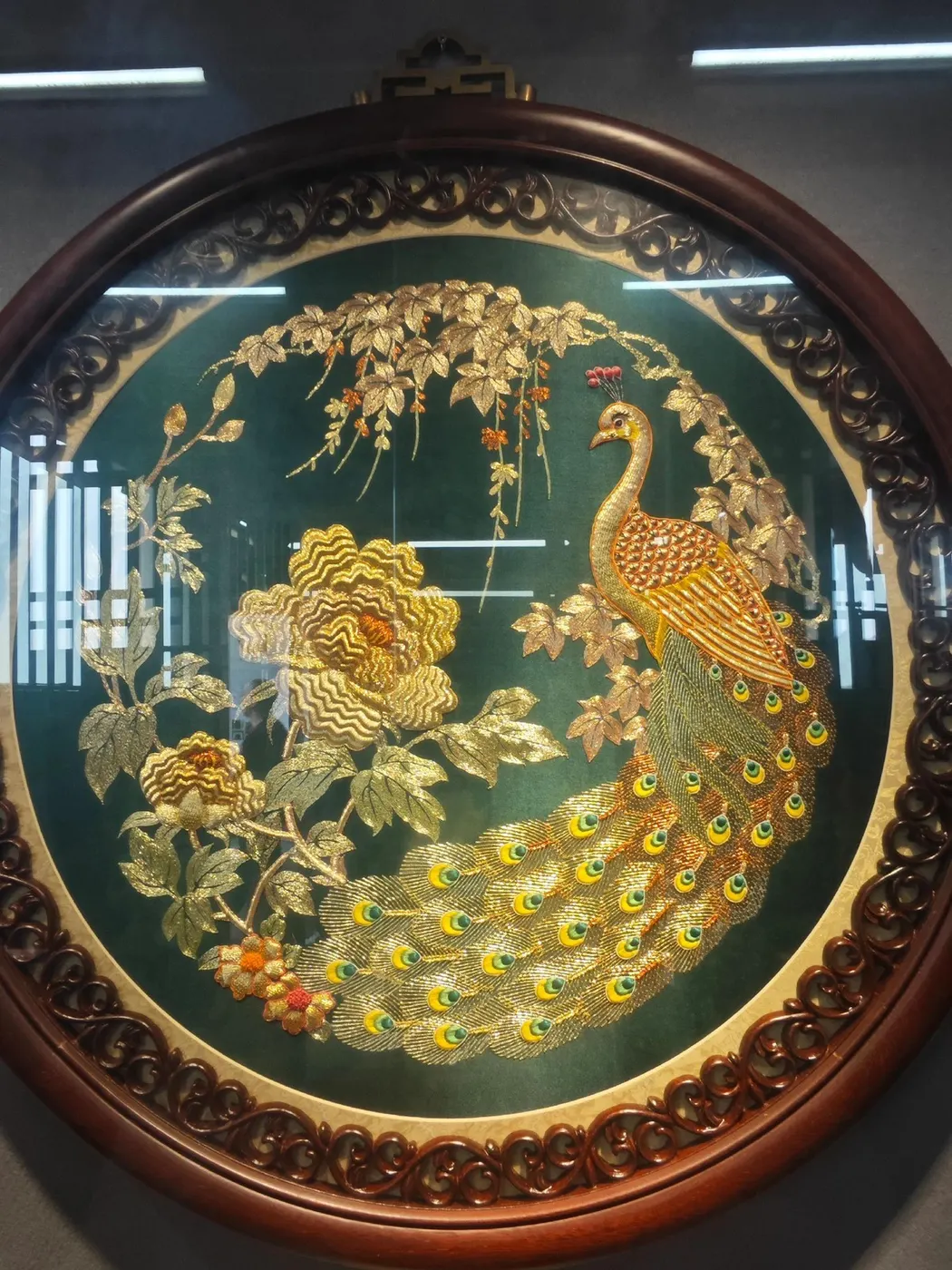 圆形绣盘内绣一只孔雀与花枝,金线勾边,玻璃有反光