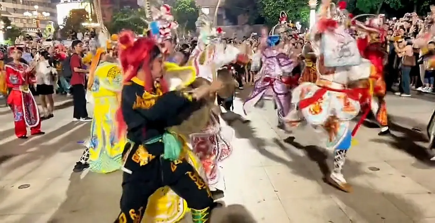 队员在街心跳起,黄衣与红衣错开,身后队伍拉成一列,路两边站满人