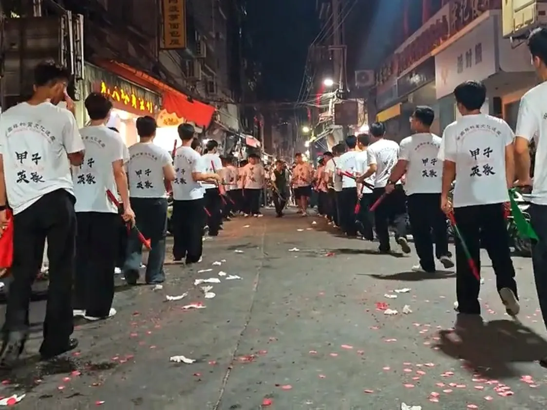 白 T 恤背後印著甲子英歌,隊伍踩著滿地紅紙往前走