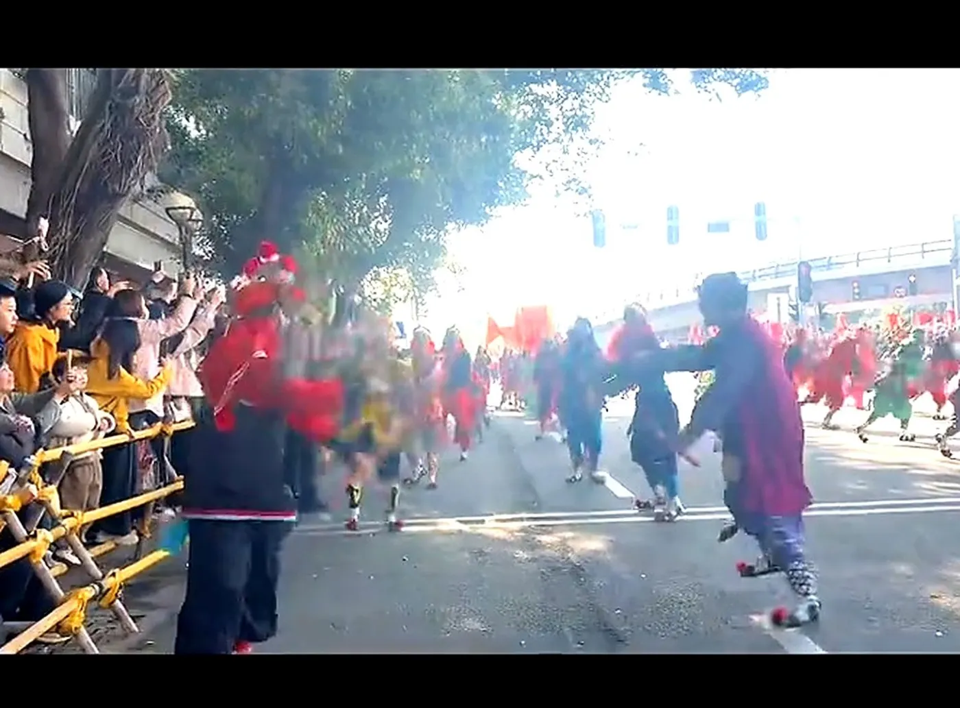 队伍在街心正面行来,队员勾脸执槌,前头有人高举旗杆,两侧站满观众