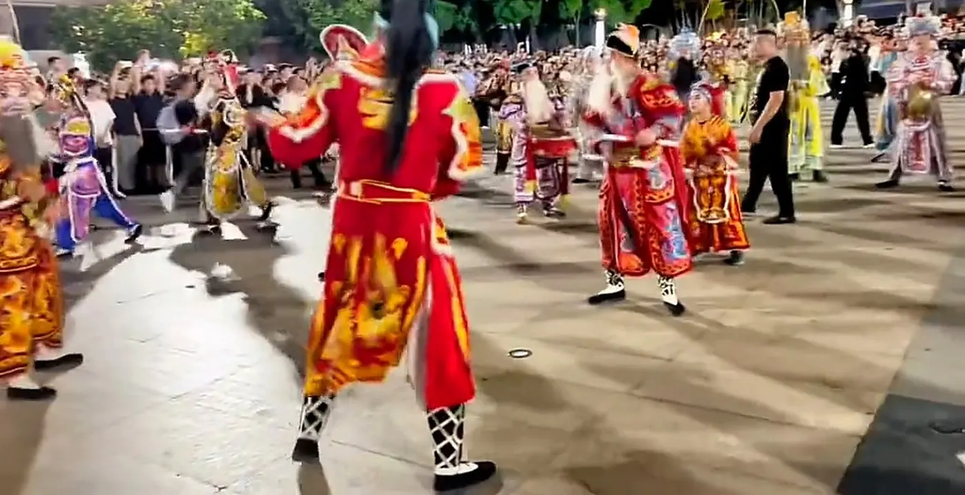 街心一支英歌队迎面推来,队员着彩色戏服、执双槌,两侧挤满围观的人