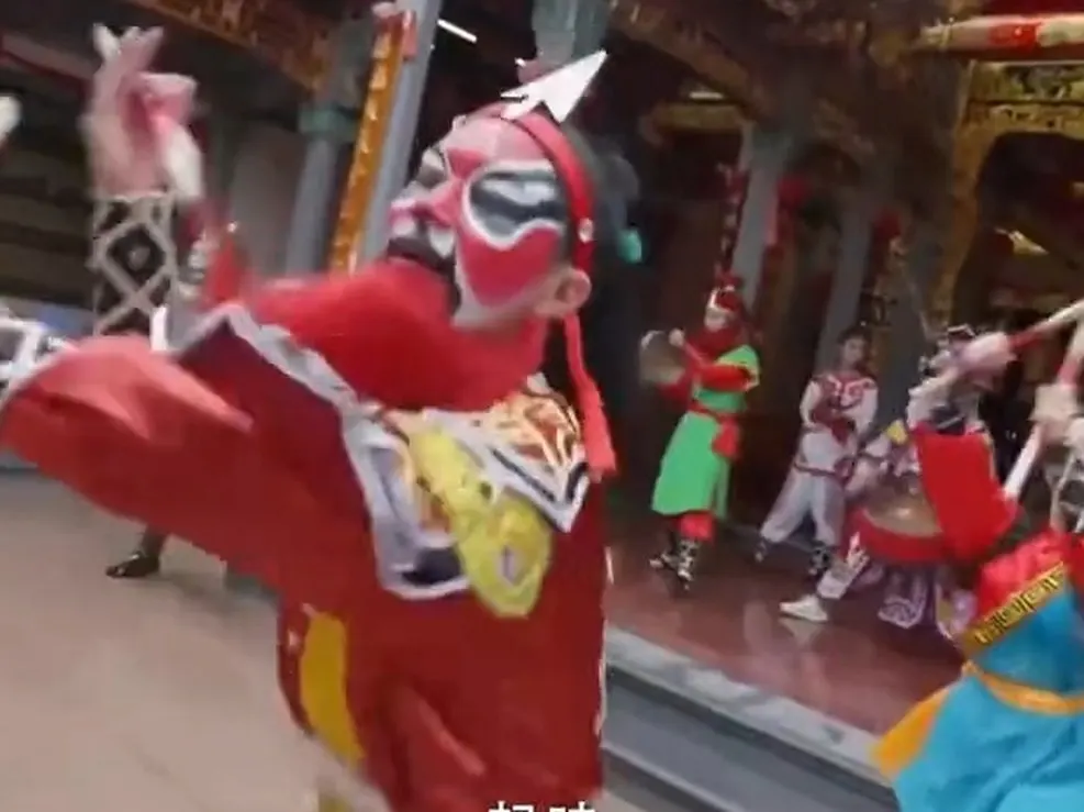 庙前一名红脸队员仰头举槌，旁边有人打钹