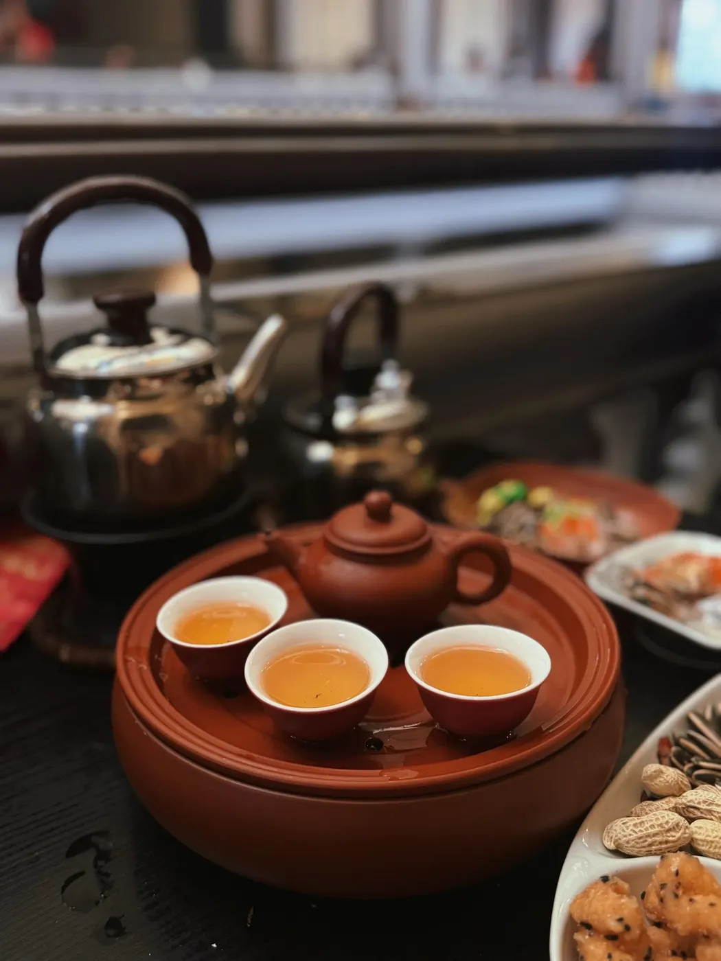 壶、三只茶杯与茶托摆在木桌上，背景虚化