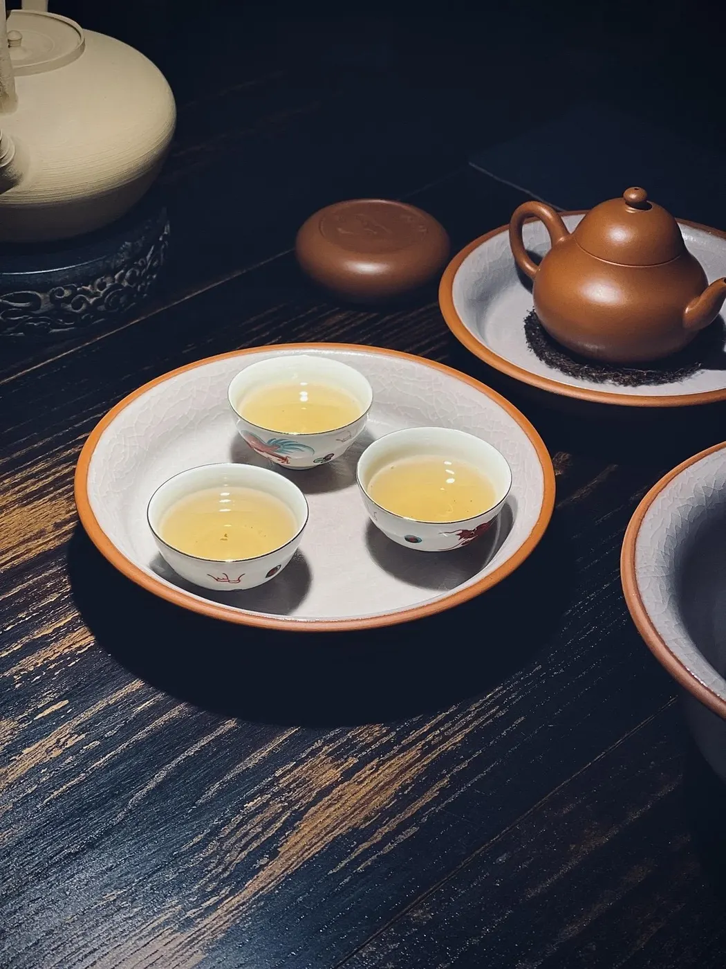 白色茶盘上三只小杯盛着茶汤，旁有紫砂壶与茶罐