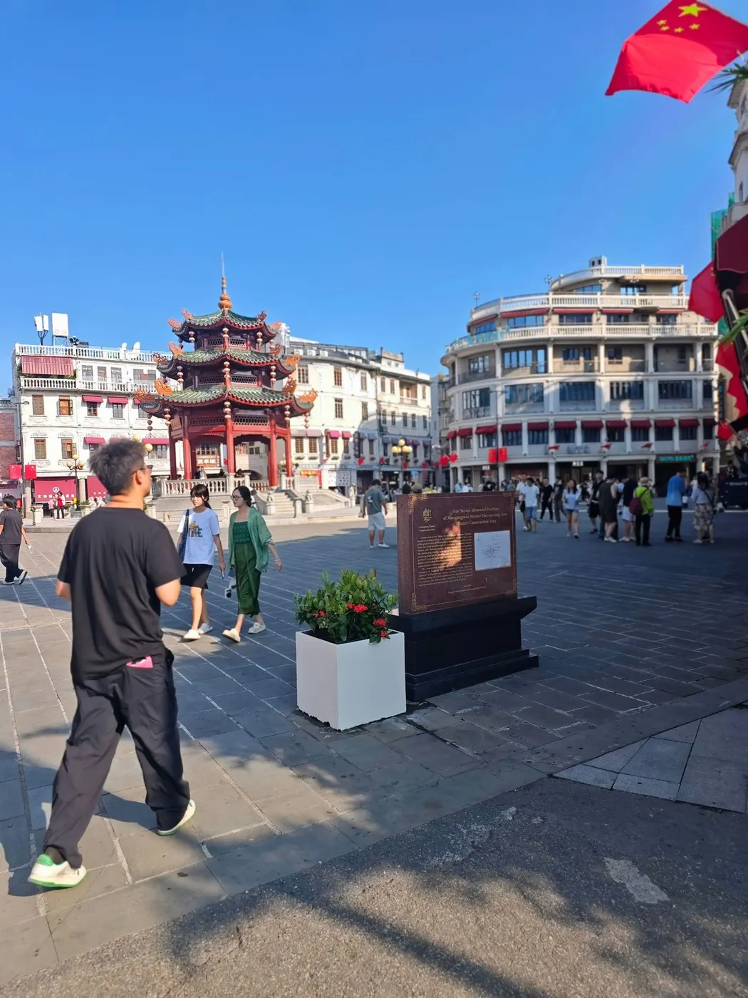 亭前的广场与步行道，四周是骑楼与行道树，有行人