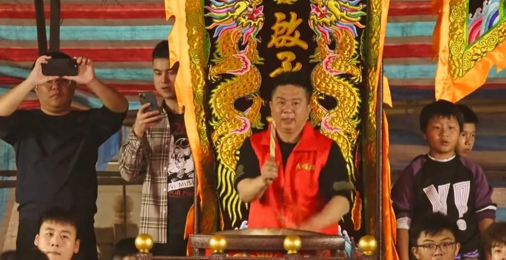 鼓师在绣双龙与「鼓」字的黑幡前举槌,鼓搁在四角带金球的木架上