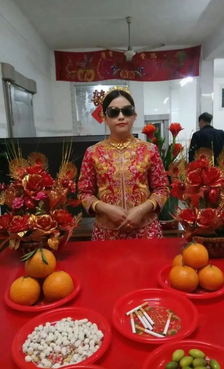 新妇穿龙凤褂立在桌前,桌上摆着柑橘、糖果、香烟和青橄榄。图源:抖音 @油条配豆浆,3 月 3 日。