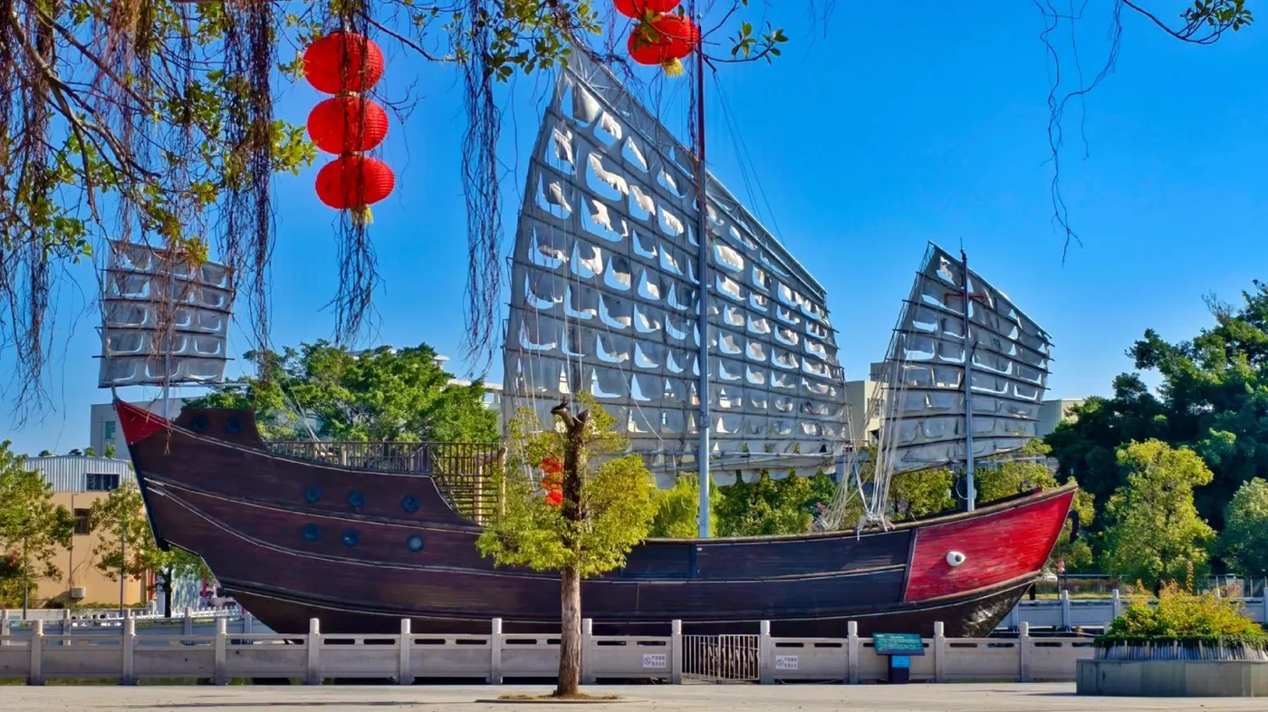 红头船立在广场上，背后是现代住宅楼与红灯笼